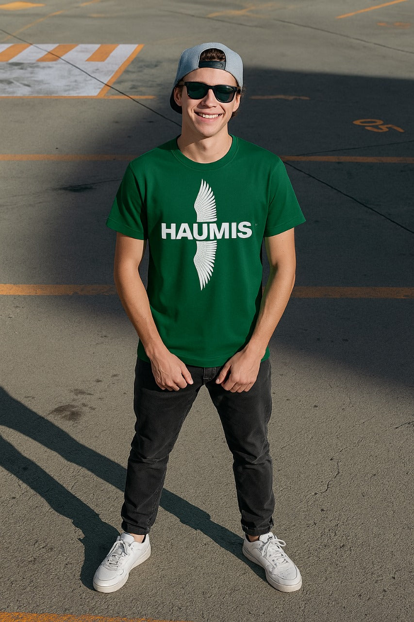 A young man wearing a Haumis Emerald Wing Tee in deep emerald green with a bold HAUMIS logo and wing graphic. Ideal for casual style.