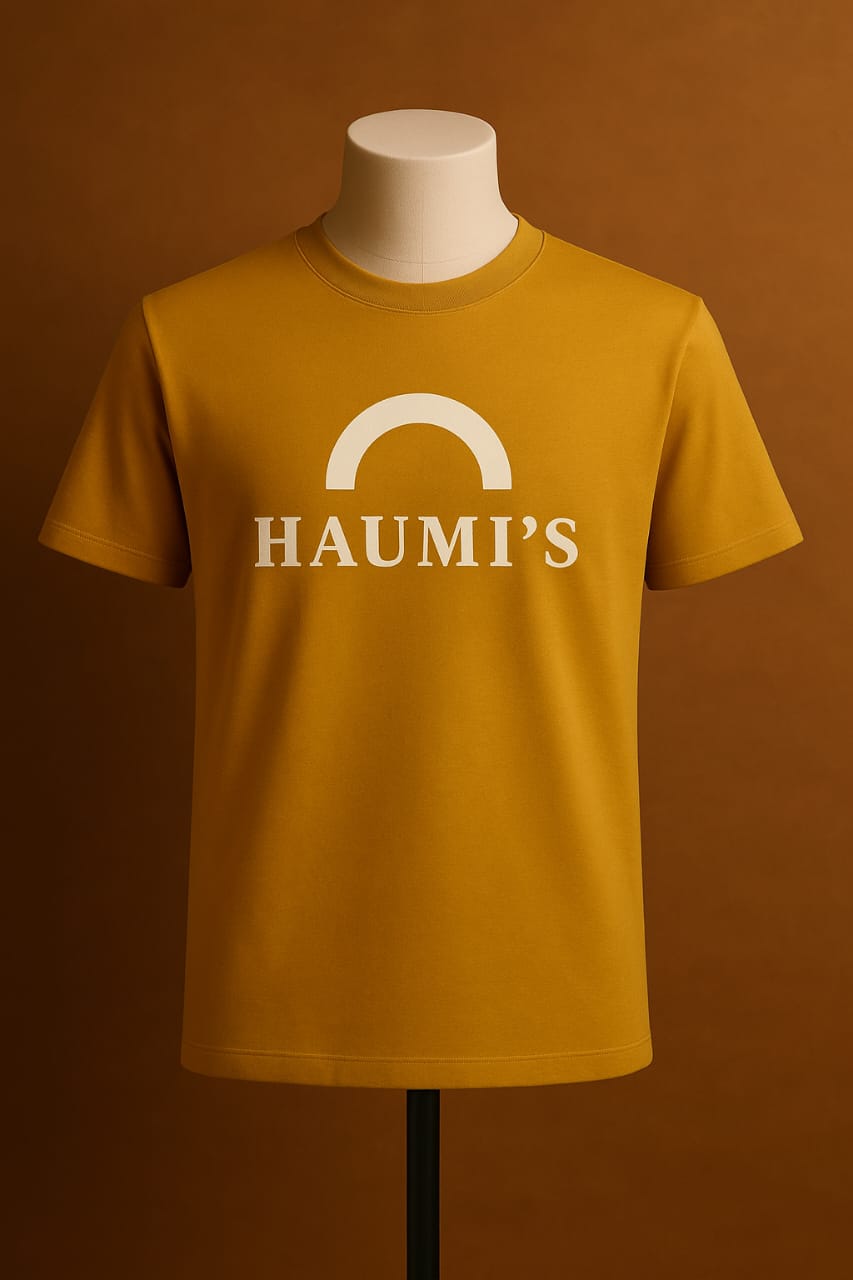 HAUMI’S Legacy Tee – Sandmark Edition in mustard yellow displayed on a mannequin with a plain brown background, highlighting the arch logo design.